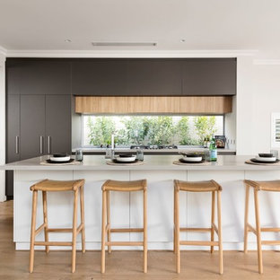 Design ideas for a contemporary galley kitchen in Perth with flat-panel cabinets, grey cabinets, window splashback, light hardwood floors, with island, brown floor and white benchtop.