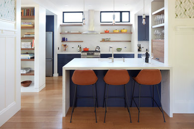 Exempel på ett litet modernt vit linjärt vitt kök med öppen planlösning, med en undermonterad diskho, släta luckor, blå skåp, bänkskiva i kvarts, vitt stänkskydd, stänkskydd i marmor, rostfria vitvaror, mellanmörkt trägolv, en halv köksö och brunt golv