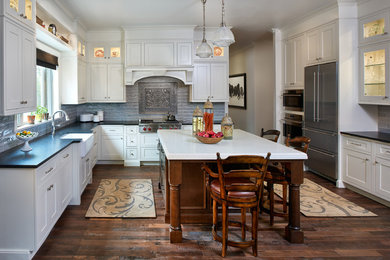 Example of a large classic u-shaped medium tone wood floor enclosed kitchen design in Denver with a farmhouse sink, beaded inset cabinets, white cabinets, quartz countertops, gray backsplash, porcelain backsplash, stainless steel appliances and an island