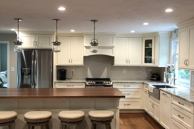 Design ideas for a medium sized traditional l-shaped kitchen/diner in Boston with a belfast sink, recessed-panel cabinets, white cabinets, engineered stone countertops, beige splashback, ceramic splashback, stainless steel appliances, dark hardwood flooring, an island and beige worktops.