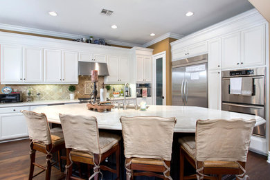 Elegant medium tone wood floor kitchen photo in San Diego with white cabinets, stainless steel appliances and an island