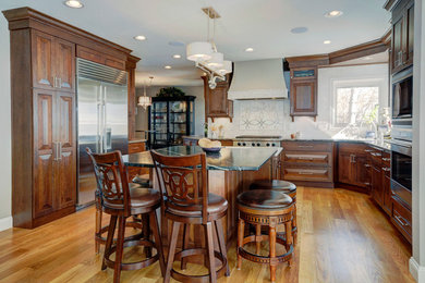 Eat-in kitchen - mid-sized traditional light wood floor eat-in kitchen idea in Denver with an undermount sink, raised-panel cabinets, dark wood cabinets, solid surface countertops, white backsplash, subway tile backsplash and white appliances