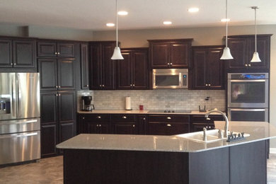 Example of a large minimalist l-shaped ceramic tile eat-in kitchen design in Other with a double-bowl sink, raised-panel cabinets, dark wood cabinets, granite countertops, gray backsplash, cement tile backsplash, stainless steel appliances and an island