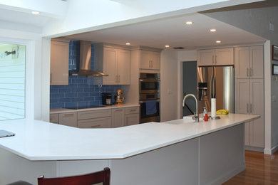 ボストンにある中くらいなトランジショナルスタイルのおしゃれなキッチン (エプロンフロントシンク、シェーカースタイル扉のキャビネット、グレーのキャビネット、クオーツストーンカウンター、青いキッチンパネル、ガラスタイルのキッチンパネル、シルバーの調理設備、無垢フローリング、ベージュの床、白いキッチンカウンター) の写真