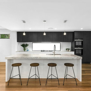 Design ideas for a large contemporary galley open plan kitchen in Brisbane with an undermount sink, dark wood cabinets, marble benchtops, white splashback, ceramic splashback, black appliances, medium hardwood floors, with island, brown floor and grey benchtop.
