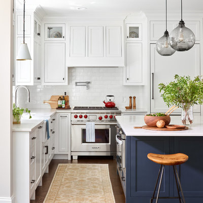 Beach style l-shaped dark wood floor kitchen photo in Boston with shaker cabinets, white cabinets, white backsplash, a farmhouse sink, subway tile backsplash, stainless steel appliances, an island and white countertops