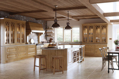 Modelo de cocina clásica grande con fregadero sobremueble, armarios con paneles empotrados, puertas de armario de madera clara, una isla y pared de piedra