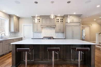 Example of a large classic u-shaped dark wood floor and brown floor kitchen design in Boston with an undermount sink, beaded inset cabinets, gray cabinets, quartz countertops, ceramic backsplash, paneled appliances, an island and beige backsplash