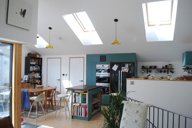 Photo of a small contemporary l-shaped kitchen/diner in Other with flat-panel cabinets, turquoise cabinets, wood worktops, black appliances, cork flooring, a breakfast bar, brown floors and brown worktops.