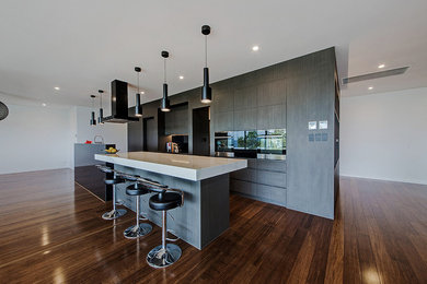 Bild på ett stort funkis kök, med en köksö, en nedsänkt diskho, skåp i mörkt trä, bänkskiva i rostfritt stål, svart stänkskydd, glaspanel som stänkskydd, svarta vitvaror och bambugolv
