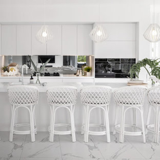 Large contemporary galley open plan kitchen in Brisbane with an undermount sink, white cabinets, quartz benchtops, black appliances, porcelain floors, with island, white floor, white benchtop, metallic splashback and mirror splashback.