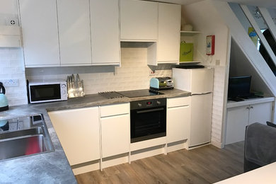 Bild på ett litet funkis kök, med en dubbel diskho, släta luckor, vita skåp, laminatbänkskiva, vitt stänkskydd, stänkskydd i tunnelbanekakel, rostfria vitvaror och vinylgolv