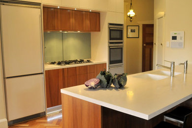 Zweizeilige, Mittelgroße Moderne Küche mit integriertem Waschbecken, flächenbündigen Schrankfronten, hellbraunen Holzschränken, Mineralwerkstoff-Arbeitsplatte, Küchenrückwand in Grün, Glasrückwand, Küchengeräten aus Edelstahl und braunem Holzboden in Perth