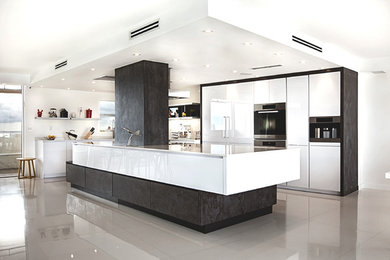 Example of a galley ceramic tile and beige floor open concept kitchen design in Miami with flat-panel cabinets, white cabinets, stainless steel appliances and an island