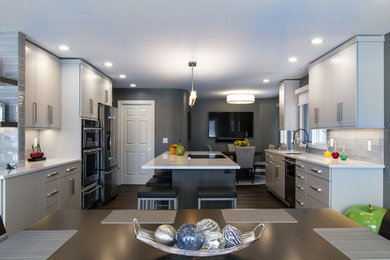 Example of a large trendy medium tone wood floor and brown floor eat-in kitchen design in Detroit with an undermount sink, flat-panel cabinets, gray cabinets, quartz countertops, gray backsplash, glass tile backsplash, stainless steel appliances, an island and white countertops