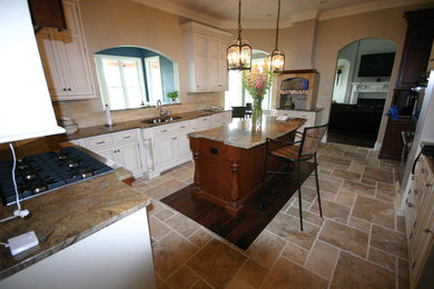 Large tuscan l-shaped travertine floor and beige floor enclosed kitchen photo in Philadelphia with a double-bowl sink, raised-panel cabinets, white cabinets, granite countertops, beige backsplash, stone tile backsplash, stainless steel appliances, an island and beige countertops