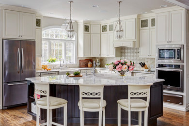 Open concept kitchen - large traditional l-shaped medium tone wood floor and brown floor open concept kitchen idea in Philadelphia with a farmhouse sink, raised-panel cabinets, white cabinets, granite countertops, gray backsplash, porcelain backsplash, stainless steel appliances and an island