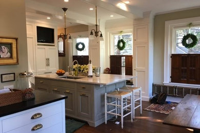 Photo of a medium sized contemporary l-shaped kitchen/diner in Philadelphia with a built-in sink, white cabinets, an island, shaker cabinets, stainless steel appliances, dark hardwood flooring and brown floors.