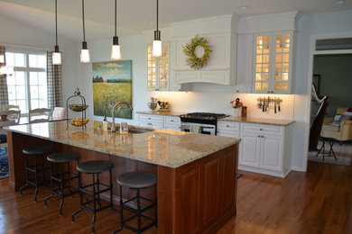 Example of a classic light wood floor kitchen design in Other with an undermount sink, raised-panel cabinets, white cabinets, granite countertops, white backsplash, subway tile backsplash, stainless steel appliances and an island