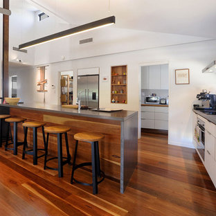 Mid-sized contemporary l-shaped kitchen in Townsville with a double-bowl sink, white cabinets, concrete benchtops, stainless steel appliances, medium hardwood floors, with island, brown floor, flat-panel cabinets and grey benchtop.