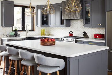 Klassische Küche in L-Form mit Landhausspüle, Glasfronten, grauen Schränken, Küchenrückwand in Weiß, Küchengeräten aus Edelstahl, Kücheninsel und weißer Arbeitsplatte in Toronto