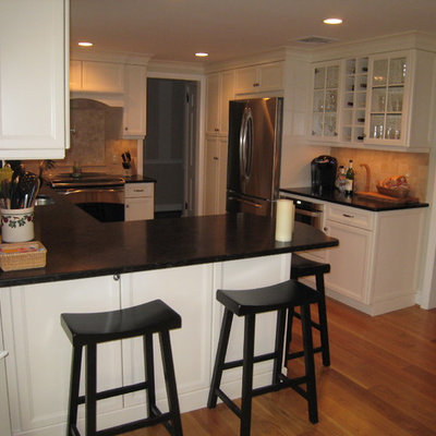 Eat-in kitchen - mid-sized transitional u-shaped medium tone wood floor eat-in kitchen idea in Bridgeport with an undermount sink, recessed-panel cabinets, white cabinets, granite countertops, beige backsplash, stone tile backsplash, stainless steel appliances, a peninsula and black countertops