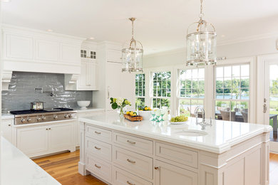 Inspiration for a large timeless l-shaped medium tone wood floor and brown floor enclosed kitchen remodel in Boston with a farmhouse sink, recessed-panel cabinets, white cabinets, marble countertops, gray backsplash, paneled appliances, an island and white countertops