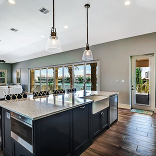 This is an example of a large transitional l-shaped open plan kitchen in Tampa with a farmhouse sink, shaker cabinets, white cabinets, recycled glass benchtops, multi-coloured splashback, porcelain splashback, stainless steel appliances, porcelain floors and with island.