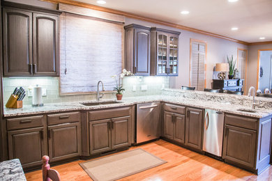 Inspiration for a large timeless u-shaped light wood floor eat-in kitchen remodel in Omaha with an undermount sink, glass-front cabinets, distressed cabinets, granite countertops, green backsplash, stainless steel appliances, a peninsula and porcelain backsplash