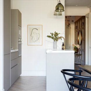 Design ideas for a contemporary galley kitchen in London with flat-panel cabinets, grey cabinets, stainless steel appliances, a breakfast bar, grey floors and white worktops.