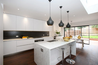 Mid-sized trendy dark wood floor eat-in kitchen photo in London with a drop-in sink, flat-panel cabinets, white cabinets, marble countertops, gray backsplash and an island