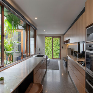 Design ideas for a mid-sized contemporary galley open plan kitchen in Melbourne with a single-bowl sink, flat-panel cabinets, medium wood cabinets, mirror splashback, panelled appliances, a peninsula, grey floor and beige benchtop.