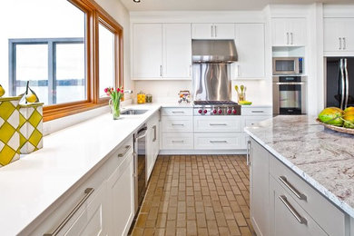 シアトルにある広いおしゃれなキッチン (ドロップインシンク、フラットパネル扉のキャビネット、白いキャビネット、大理石カウンター、白いキッチンパネル、シルバーの調理設備、レンガの床) の写真
