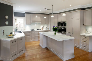 Inredning av ett modernt mellanstort kök, med en dubbel diskho, skåp i shakerstil, vita skåp, marmorbänkskiva, vitt stänkskydd, glaspanel som stänkskydd, rostfria vitvaror, mellanmörkt trägolv och en köksö
