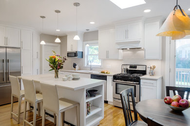 Inspiration for a mid-sized transitional u-shaped light wood floor enclosed kitchen remodel in Boston with a drop-in sink, shaker cabinets, white cabinets, laminate countertops, white backsplash, subway tile backsplash, stainless steel appliances and an island