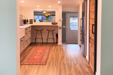 Small trendy galley light wood floor and beige floor enclosed kitchen photo in Seattle with a farmhouse sink, gray cabinets, solid surface countertops, white backsplash, subway tile backsplash, stainless steel appliances and white countertops