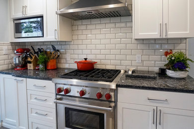 Mid-sized trendy l-shaped vinyl floor and gray floor enclosed kitchen photo in Seattle with an undermount sink, shaker cabinets, white cabinets, granite countertops, white backsplash, ceramic backsplash, stainless steel appliances and blue countertops