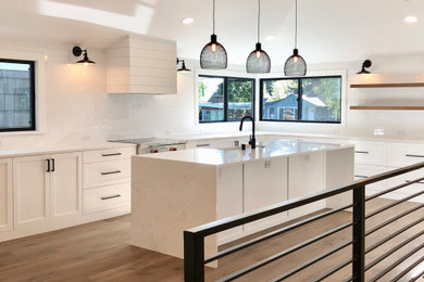 Example of a country light wood floor and brown floor kitchen design in Seattle with a farmhouse sink, shaker cabinets, white cabinets, quartzite countertops, white backsplash, ceramic backsplash, stainless steel appliances, an island and white countertops