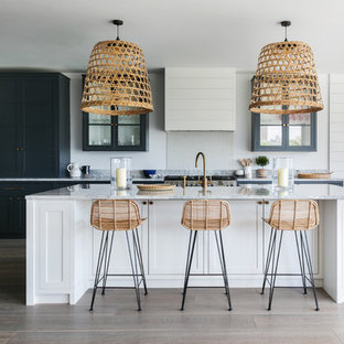 Inspiration for an expansive beach style open plan kitchen in London with glass-front cabinets, blue cabinets, stainless steel appliances, light hardwood flooring, an island, grey worktops and granite worktops.