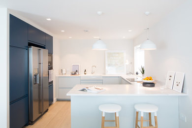 Photo of a medium sized contemporary u-shaped open plan kitchen in Sussex with a belfast sink, blue cabinets, quartz worktops, white splashback, integrated appliances, a breakfast bar and flat-panel cabinets.