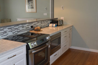 Example of a transitional single-wall medium tone wood floor open concept kitchen design in Boston with a single-bowl sink, white cabinets, marble countertops, multicolored backsplash, mosaic tile backsplash, stainless steel appliances, a peninsula and raised-panel cabinets