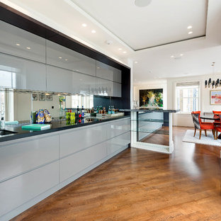 Contemporary single-wall kitchen in London with a double-bowl sink, flat-panel cabinets, blue cabinets, mirror splashback, medium hardwood flooring, brown floors and black worktops.