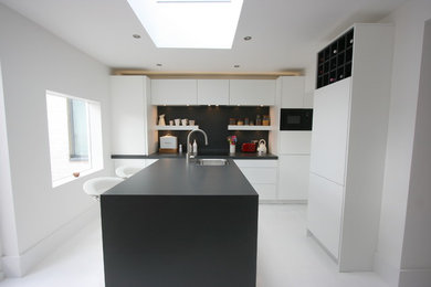 Design ideas for a medium sized modern l-shaped kitchen/diner in London with a built-in sink, flat-panel cabinets, white cabinets, laminate countertops, black splashback, black appliances, an island and painted wood flooring.