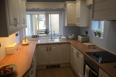 Small classic u-shaped enclosed kitchen in Other with a built-in sink, shaker cabinets, beige cabinets, wood worktops, stainless steel appliances, light hardwood flooring and no island.
