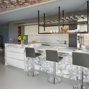 This is an example of an expansive contemporary single-wall open plan kitchen in London with flat-panel cabinets, white cabinets, marble worktops, white splashback, stone slab splashback, black appliances, an island, grey floors, white worktops and an integrated sink.
