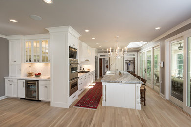Klassisk inredning av ett stort linjärt kök med öppen planlösning, med en rustik diskho, släta luckor, vita skåp, marmorbänkskiva, vitt stänkskydd, stänkskydd i keramik, rostfria vitvaror, ljust trägolv och en köksö