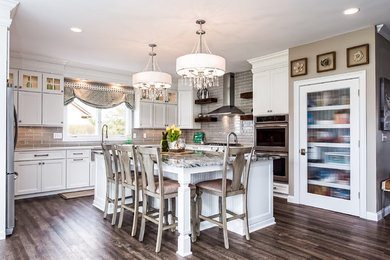 Mid-sized elegant l-shaped brown floor eat-in kitchen photo in Columbus with a farmhouse sink, recessed-panel cabinets, white cabinets, quartz countertops, gray backsplash, glass tile backsplash, stainless steel appliances and an island