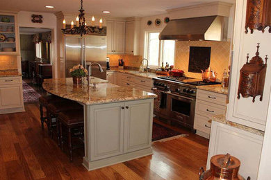 Eat-in kitchen - mid-sized traditional l-shaped medium tone wood floor eat-in kitchen idea in Indianapolis with raised-panel cabinets, yellow backsplash, ceramic backsplash, stainless steel appliances, an island, a farmhouse sink, laminate countertops and white cabinets
