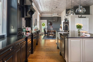 Example of a large classic l-shaped medium tone wood floor and beige floor open concept kitchen design in Toronto with a farmhouse sink, raised-panel cabinets, black cabinets, quartz countertops, gray backsplash, subway tile backsplash, stainless steel appliances and an island