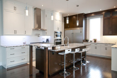Example of a large transitional u-shaped dark wood floor and brown floor kitchen design in Calgary with an undermount sink, shaker cabinets, white cabinets, granite countertops, white backsplash, subway tile backsplash, stainless steel appliances and an island